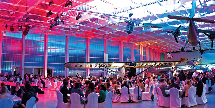 Eine stimmungsvoll beleuchtete Eventlocation mit Partygästen und Bühnenbeleuchtung.