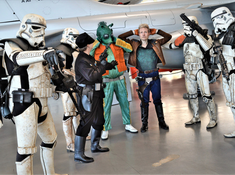Star-Wars-Kostüme im Hangar Mehrere Personen in Star-Wars-Kostümen im Hangar mit Flugzeugen im Hintergrund.