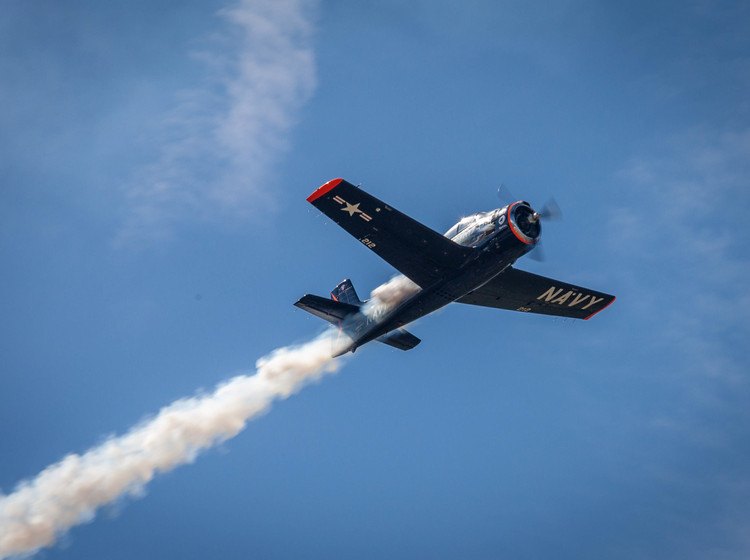 Flugshow Ein Flugzeug vor blauem Himmel fliegt quer durch das Bild.
