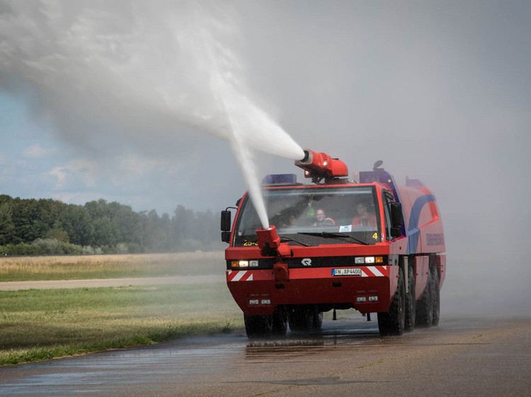 Flughafen-Feuerwehr im Einsatz Ein Flughafen-Feuerwehrfahrzeug von Vorne spritzt große Wassermassen auf das Rollfeld.