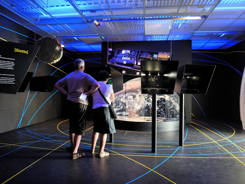 Zwei Personen betrachten interaktive Displays in einem futuristisch gestalteten Ausstellungsraum mit blauem Licht und Raumfahrtthema im Dornier Museum