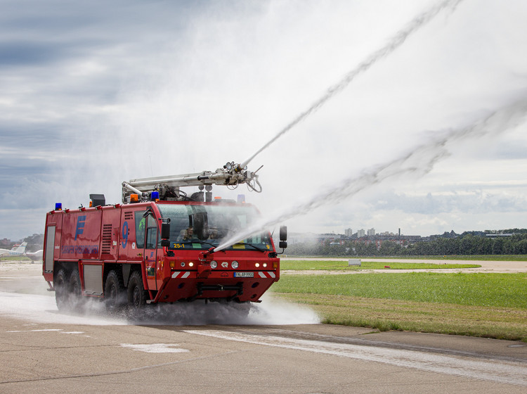 Flughafen-Feuerwehr im Einsatz Ein Flughafen-Feuerwehrfahrzeug spritzt Wasser auf das Rollfeld.