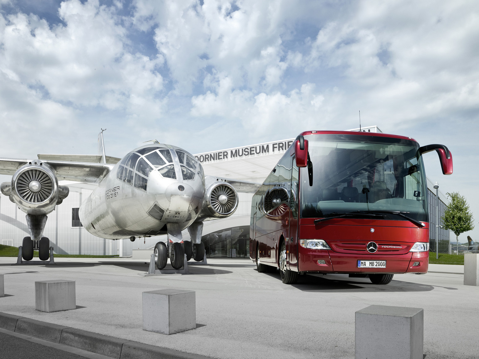 Busgruppen Ausflugsziel A silver plane in front of the Dornier Museum with a big red coach on the right of the picture.